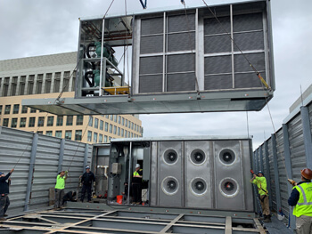  EMCOR Services Northeast workers lowering a mechanical unit with a crane